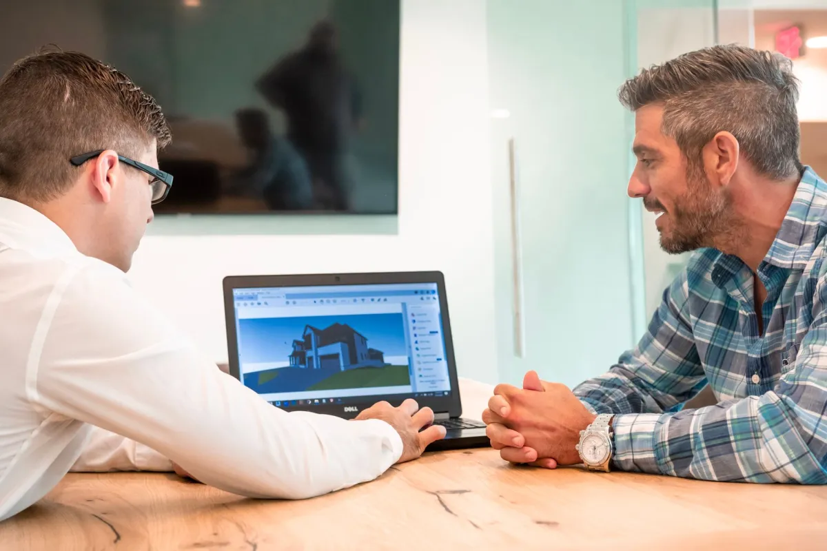 Two professionals discussing a 3D architectural design on a laptop in a modern office