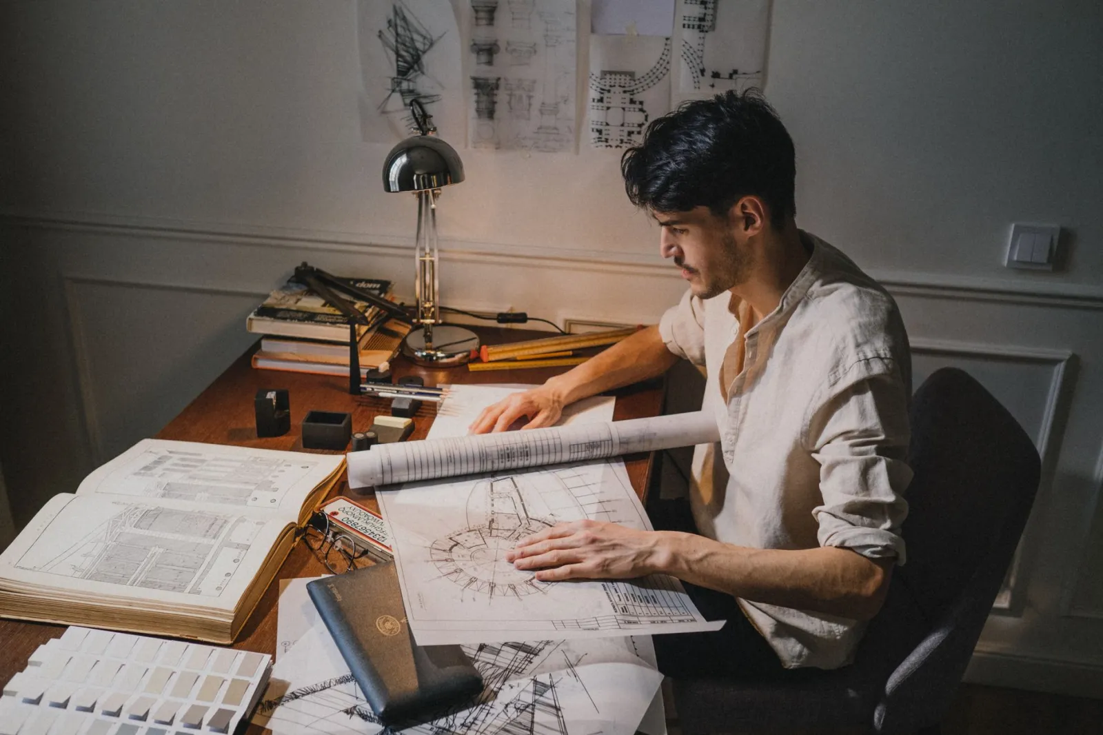 Young architect working on blueprint designs at a desk under lamp light