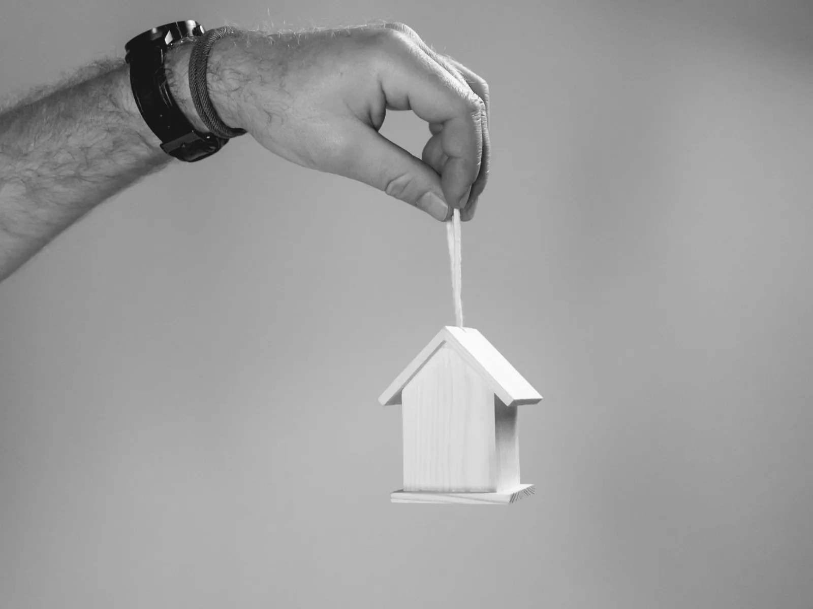 Hand holding a small wooden house model by a string in black and white