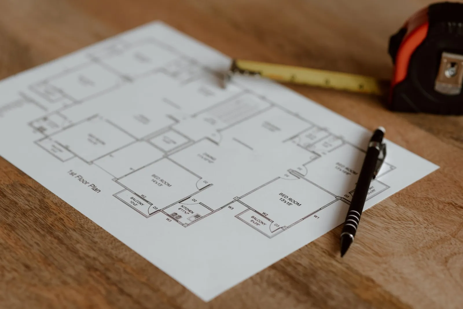 Architectural floor plan on paper placed on a wooden surface near a pen and ruler